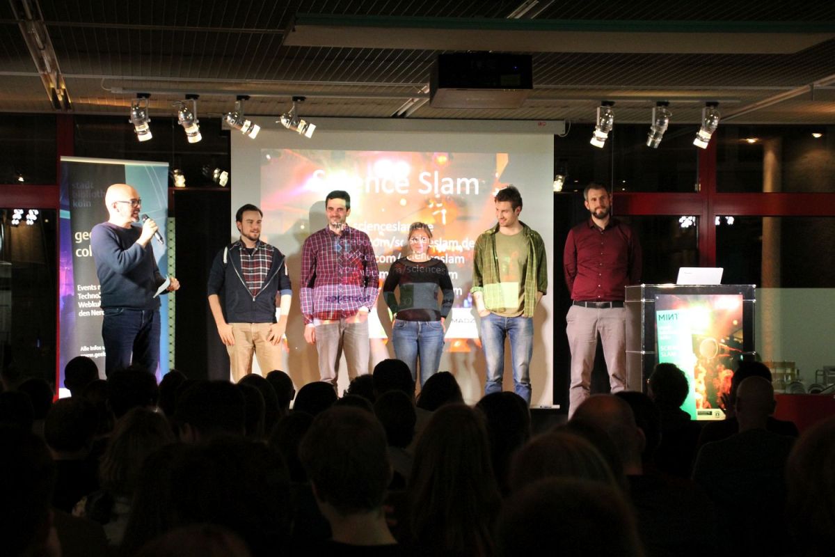Die beleuchtete Bühne der Zentralbibliothek. Im dunklen Vordergrund das Publikum. Auf der Bühne stehen nebeneinander der Moderator, 4 Slammer und eine Slammerin.