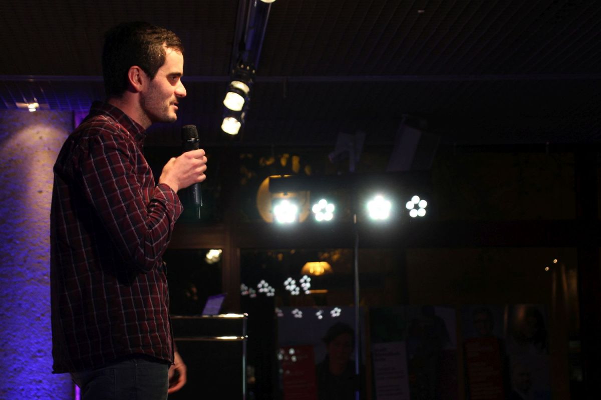 Ein junger Mann von der Seite fotografiert. Er spricht in ein Mikrofon.