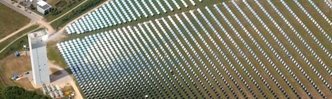 Luftbild von schräg oben: DLR-Solarturm in Jülich mit einem Feld aus über 2000 Spiegeln, die das Sonnenlicht auf den Turm lenken. Drumherum Wiesen und Felder, nur wenig Bebauung.